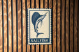 A metal sign with a blue and white design featuring a sailfish is mounted on a wooden wall.