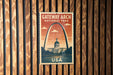 A vintage-style postage stamp featuring the Gateway Arch, a famous landmark in the United States, is displayed on a wooden wall.