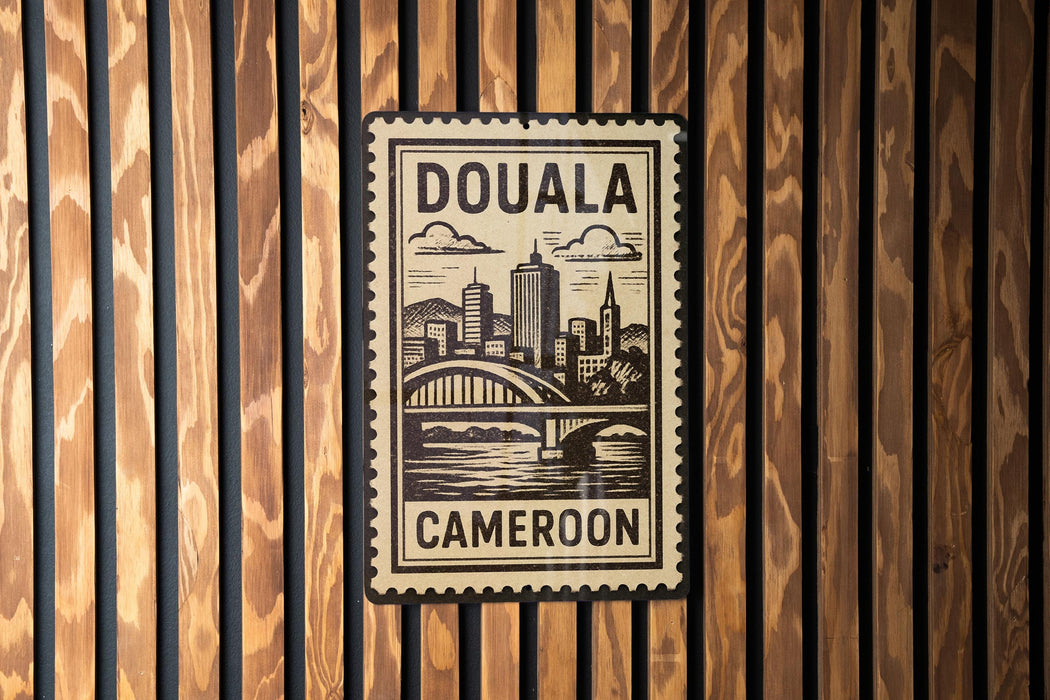 a stamp-like sign with the text "DOUALA CAMERON" and a cityscape illustration, mounted on a wooden wall.