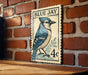 A vintage postage stamp featuring a blue jay, mounted on a brick wall.