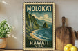 A framed vintage-style stamp depicting a mountainous landscape with a beach and ocean, placed on a shelf next to a wooden cutting board and some lemons.