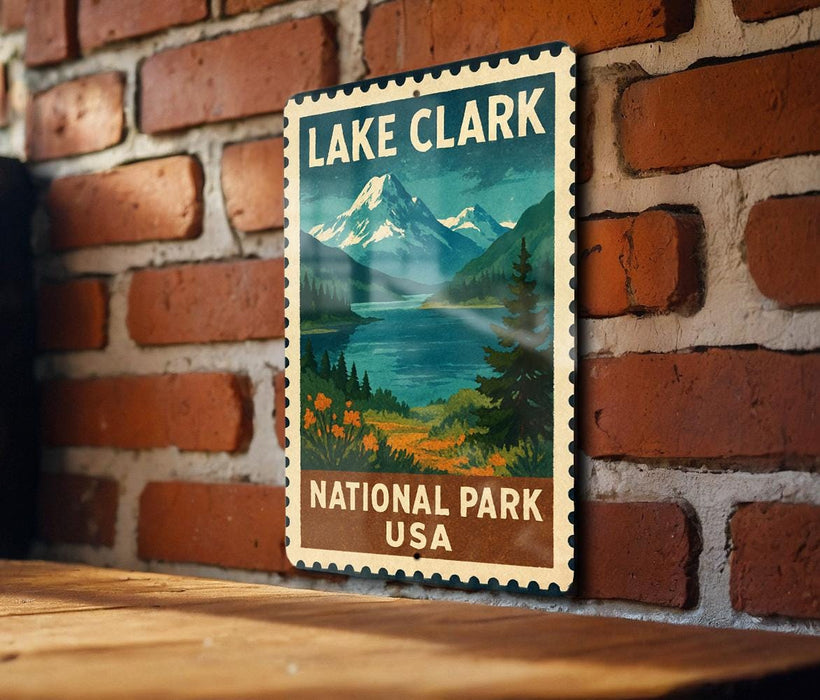 A vintage-style metal sign for Lake Clark National Park in the United States, featuring a scenic mountain landscape with a lake and pine trees.