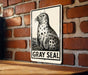 A sign featuring a black and white illustration of a gray seal against a brick wall.
