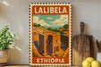 A vintage-style metal sign with the text "LALIBEA" and "ETHIOPIA" printed on it, depicting a building in Ethiopia. The sign is displayed on a shelf next to a potted plant, a wooden cutting board, and some lemons.