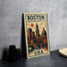 A vintage-style metal sign depicting the Boston, Massachusetts, USA skyline, with a clock tower and other iconic buildings, is displayed on a gray concrete surface.