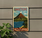 A vintage-style metal sign with a colorful illustration of a mountain, a lake, and palm trees, mounted on a gray wall.