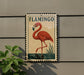 A framed illustration of a flamingo is displayed on a wall, with a plant to the left.