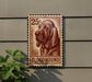 a 25¢ postage stamp with a bloodhound illustration, mounted on a wall next to a plant.