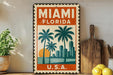 A vintage-style metal sign with the text "MIAMI FLORIDA U.S.A." displayed prominently, featuring palm trees and a sunset. The sign is placed on a shelf next to a wooden cutting board and a potted plant.
