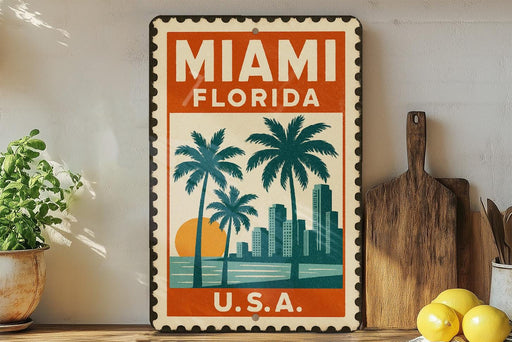 A vintage-style metal sign with the text "MIAMI FLORIDA U.S.A." displayed prominently, featuring palm trees and a sunset. The sign is placed on a shelf next to a wooden cutting board and a potted plant.