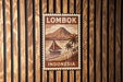 A vintage postage stamp from Indonesia featuring a sailboat on a beach with a mountain in the background.