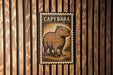 a metal sign with a picture of a capybara, a type of rodent, mounted on a wooden wall.
