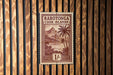 a brown and white postage stamp from the Cook Islands, with a tropical landscape and palm trees depicted on it.