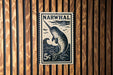 A black and white postage stamp featuring a narwhal, a type of whale, is displayed on a wooden wall.