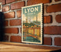 A vintage-style postage stamp depicting the city of Lyon, France, with a bridge and buildings in the background.