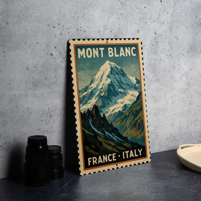 A vintage-style metal sign with a mountain landscape and the text "MONT BLANC FRANCE ITALY" is displayed on a gray concrete surface.