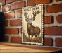 A wooden table with a framed image of a mule deer on it, mounted on a brick wall.