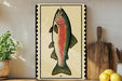 a framed illustration of a colorful fish, possibly a rainbow trout, on a wooden surface.