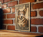 A wooden frame with a vintage-style stamp featuring a Corgi dog on a brick wall.