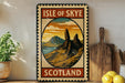 A vintage-style metal sign with the text "ISLE OF SKYE SCOTLAND" and an illustration of a mountainous landscape, placed on a wooden surface next to a potted plant and a wooden cutting board.