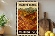 A framed poster of a mountainous landscape with the text "Zhangye Dania" and "CHINA 20" printed on it, placed on a shelf next to a wooden cutting board and a potted plant.