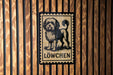 A black and white illustration of a dog is displayed on a wooden wall, with the word "LÖWCÖN" written below it.