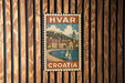 A vintage-style metal stamp depicting a coastal town in Croatia, with a sailboat on the water and buildings along the shore.