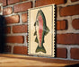 a brick wall with a framed illustration of a fish on it.