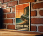 A vintage-style postage stamp depicting a tropical beach scene with a cliff overlooking the ocean, hanging on a brick wall.