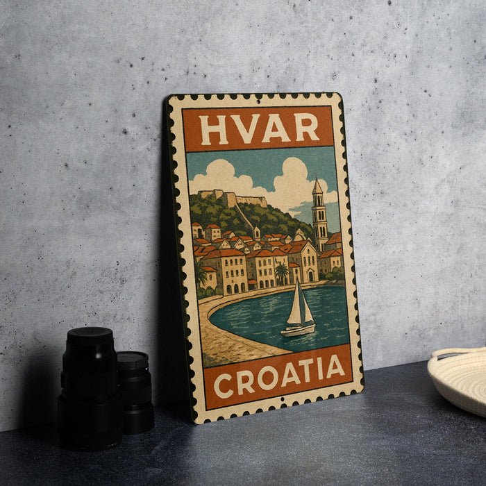 a vintage-style metal stamp depicting a coastal town in Croatia, with a sailboat on the water and a castle in the background.