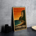 A vintage-style metal sign with a tropical island landscape, featuring a cliff overlooking the ocean, is displayed on a gray countertop.