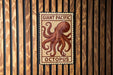 a sign with an illustration of an octopus, mounted on a wooden wall.