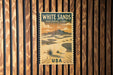 A vintage-style poster for White Sands National Park in the United States, featuring a desert landscape with mountains and a palm tree.