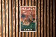 A vintage-style postage stamp from Spain featuring a building and palm trees, mounted on a wooden wall.
