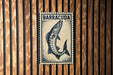 A framed image of a fish, specifically a barracuda, is displayed on a wooden wall.