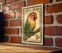 A vintage postage stamp featuring a colorful parrot perched on a branch, with the text "LOVE BIRD" and a value of 5 cents.