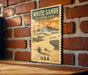 A vintage-style poster of White Sands National Park, featuring a desert landscape with mountains and a cactus in the foreground, is displayed on a brick wall.
