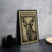 A metal plate with a black and white illustration of a horned animal, possibly a goat or ram, is displayed on a table.