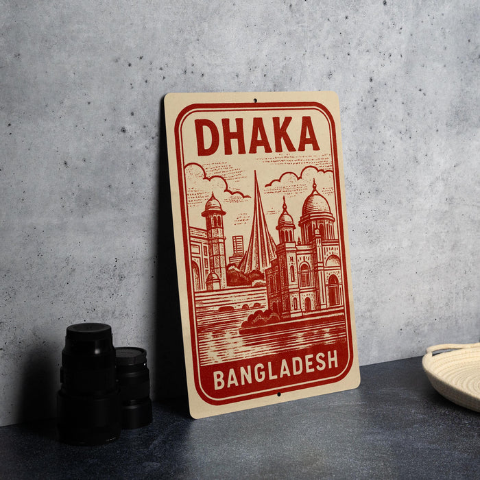 A red and white sign with the text "Dhaka Bangladesh" is displayed on a gray countertop, accompanied by a stack of black camera lenses and a woven basket.