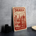 A red and white sign with the text "Dhaka Bangladesh" is displayed on a gray countertop, accompanied by a stack of black camera lenses and a woven basket.