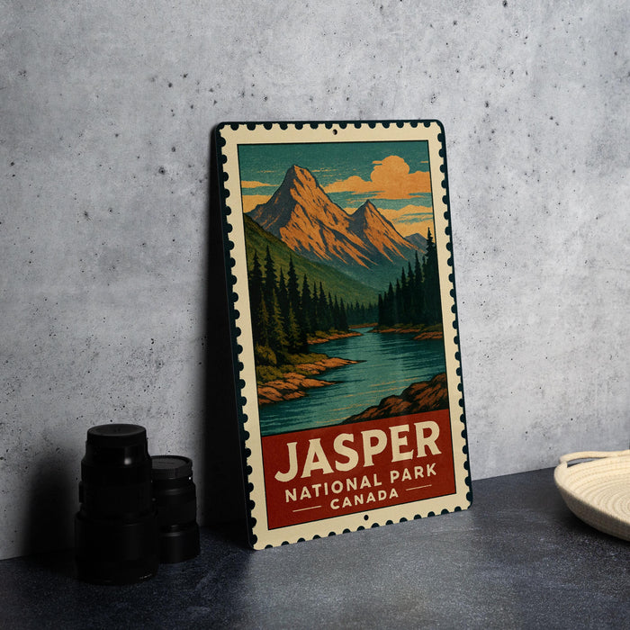 A vintage-style metal sign depicting a scenic landscape with mountains, a river, and pine trees, with the text "JASPER NATIONAL PARK CANADA" printed on it.