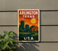 A vintage-style metal sign with the text "ARLINGTON TEXAS USA" displayed on a wall, featuring an illustration of a city skyline and a sunset.