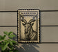a metal sign with a black and white illustration of a horned animal, possibly a goat or ram, mounted on a wall.