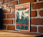 A vintage-style poster of Manchester, England, featuring a cityscape with a clock tower and other architectural elements, mounted on a brick wall.