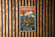 A vintage-style metal stamp with the text "ZARAGOZA SPAIN" and an illustration of a cityscape with a bridge.