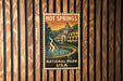A vintage-style poster for Hot Springs National Park in the United States, featuring a building and a fountain in the background.