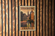 A vintage-style metal sign with the text "STRASBOURG FRANCE" displayed on a wooden wall.