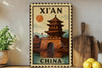 A vintage-style stamp depicting a traditional Chinese temple, with the text "XI'AN CHINA" prominently displayed. The stamp is placed on a shelf next to a wooden cutting board and a potted plant, creating a decorative and cultural-themed display.