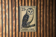A 25c postage stamp featuring a barn owl is displayed on a wooden wall.