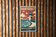 A vintage-style metal sign with a lighthouse and ocean scene, mounted on a wooden wall.